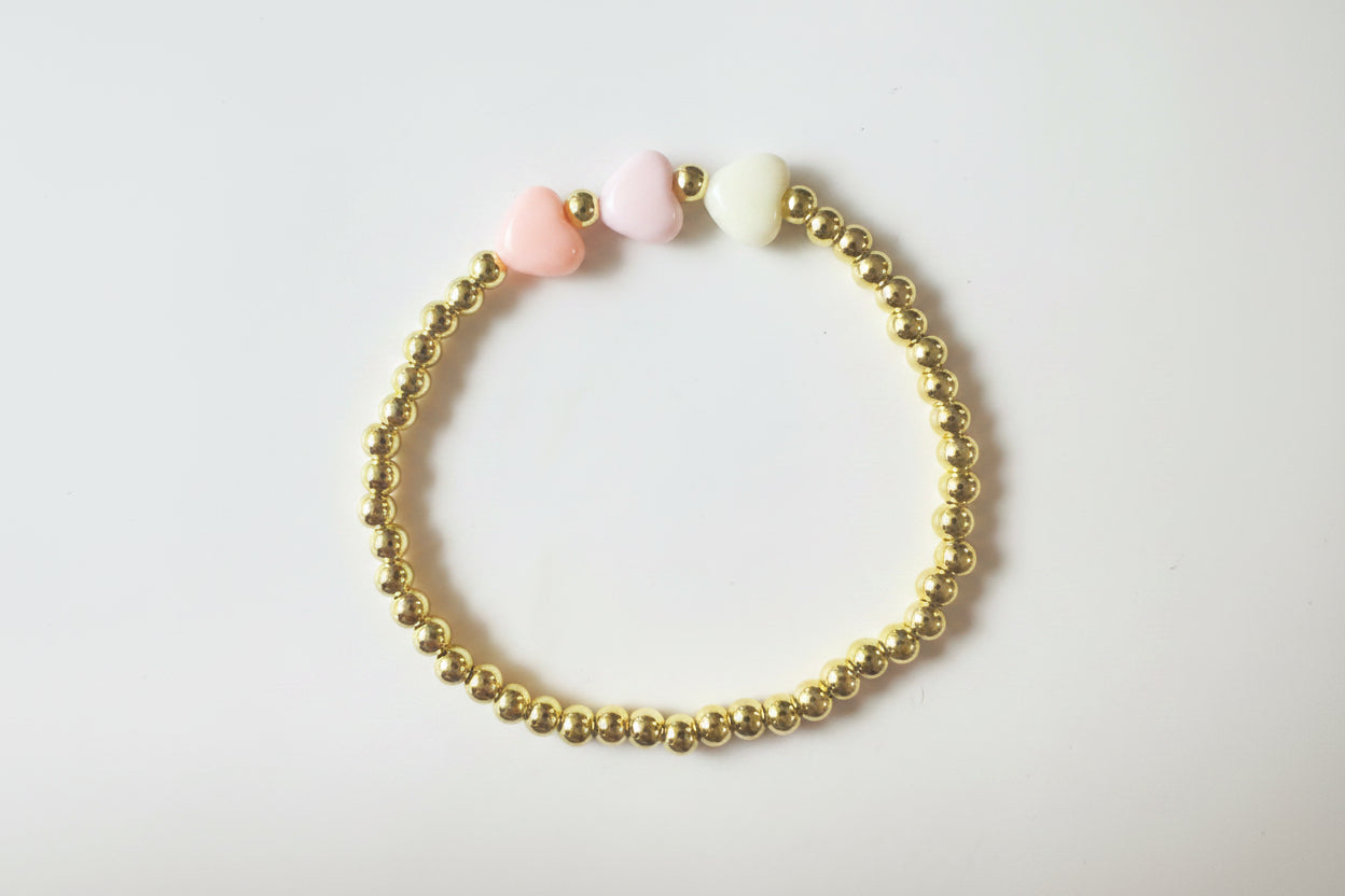 Gold beaded bracelet with pink and white beads on a light background